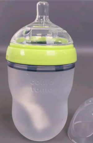 Silicone baby bottle with green rim and 'comotomo' branding on a gray background
