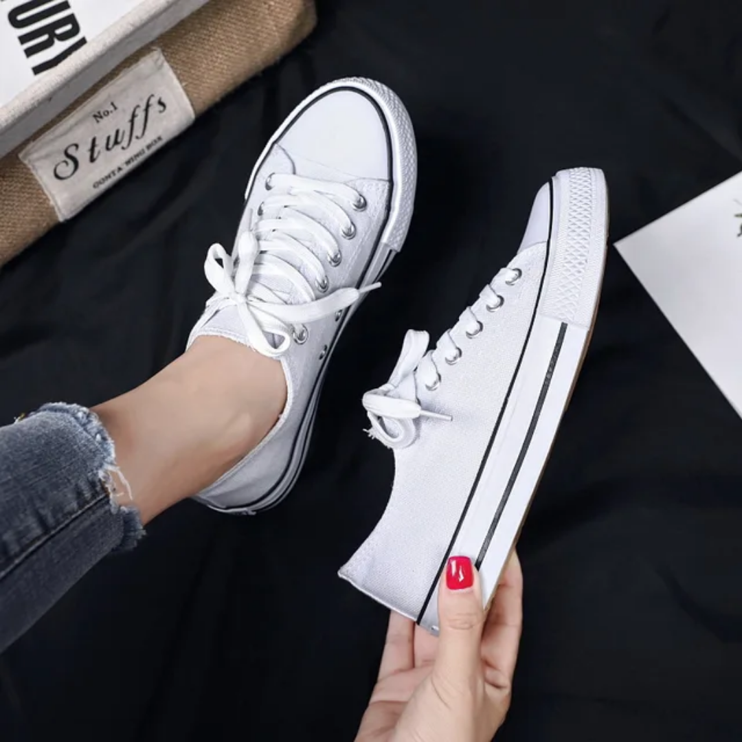 White sneakers being held by a person with a dark background
